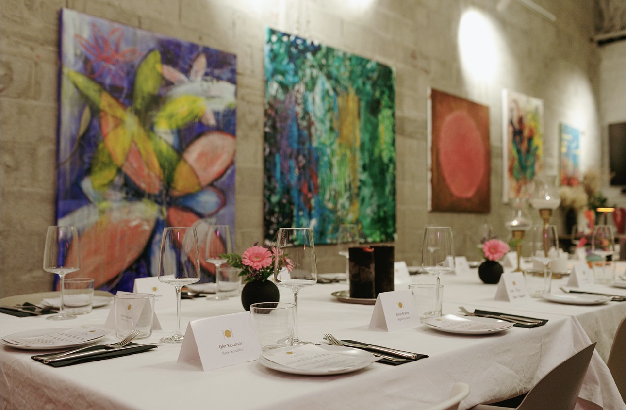 Installation view of Reversing by Nili Stein at BUBU, Tel Aviv, with paintings hung along the wall behind a long dining table